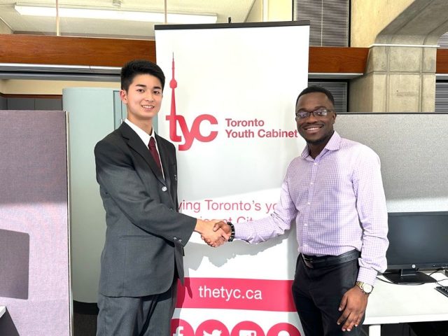 Toronto Youth Cabinet のバナーの前で、代表と握手を交わすTEIGEN JP代表