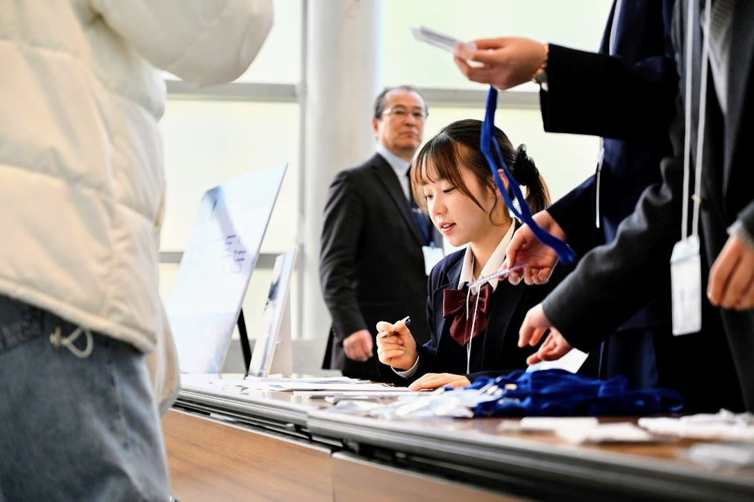 受付のテーブルで、メンバーが来場者に名札を渡しながら応対している様子