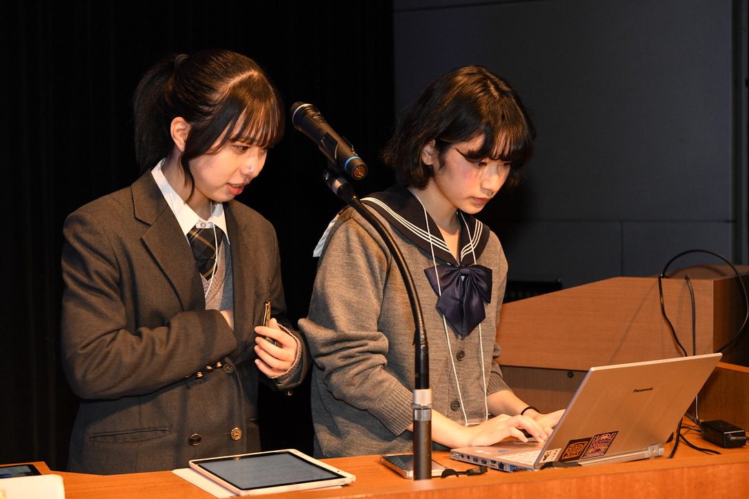 モギ区長選の進行席で、2人のメンバーがノートパソコンとマイクを操作している様子