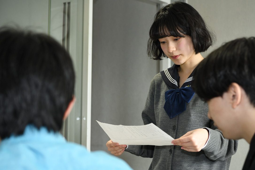 1枚の進行台本を手に、メンバー3人が読み合わせをしている様子