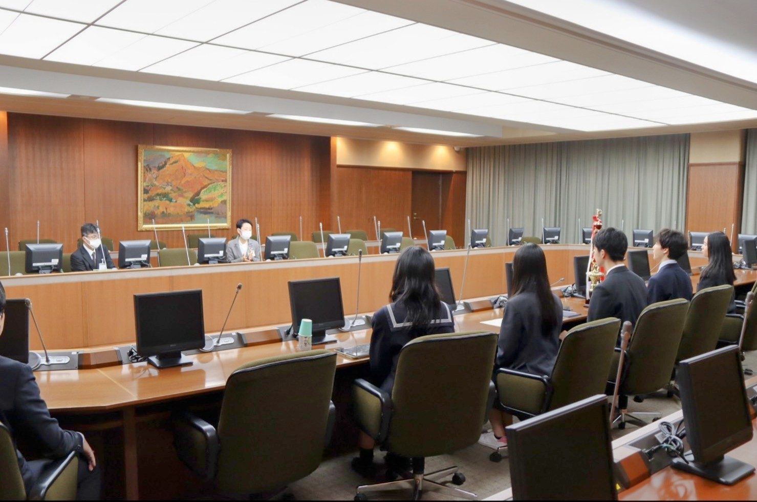 トロフィーを置いた会議室の席で、向かいに座る大人の話を聞くメンバー